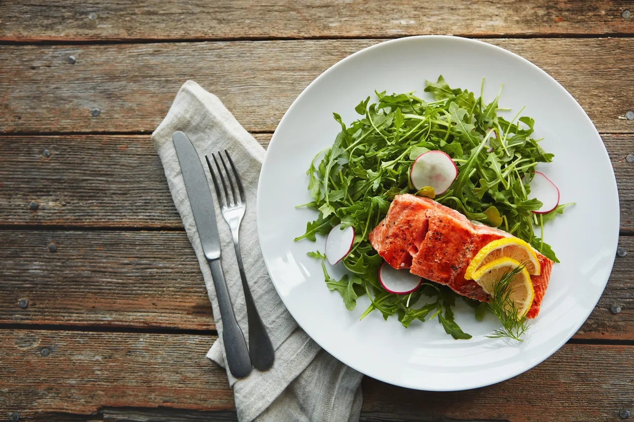 A plate of grilled salmon on an arugula salad — a palm-sized protein portion anchoring a meal.