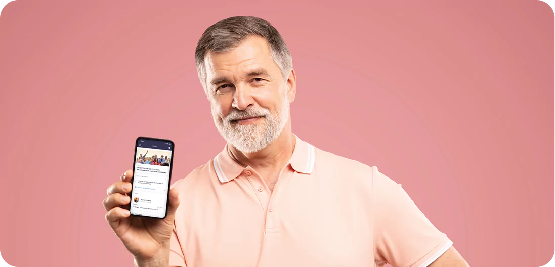 Middle-aged bearded man holding smartphone toward camera, pointing at the device displaying the Constant Health app Home screen.
