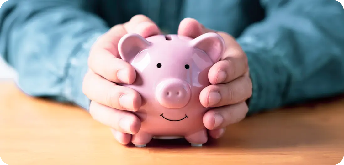 Close-up of a man's hands clasped around a pink piggy bank resting on a table—symbolizing saving and financial mindfulness.